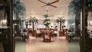 A spacious dining area with a central round table, surrounded by chairs, and palm trees.