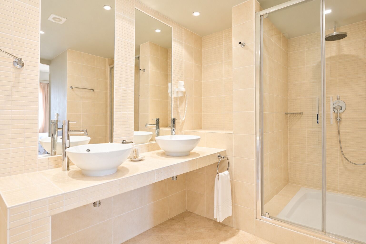 Un baño moderno con dos lavamanos, una ducha con cerramiento de vidrio y un espejo grande.