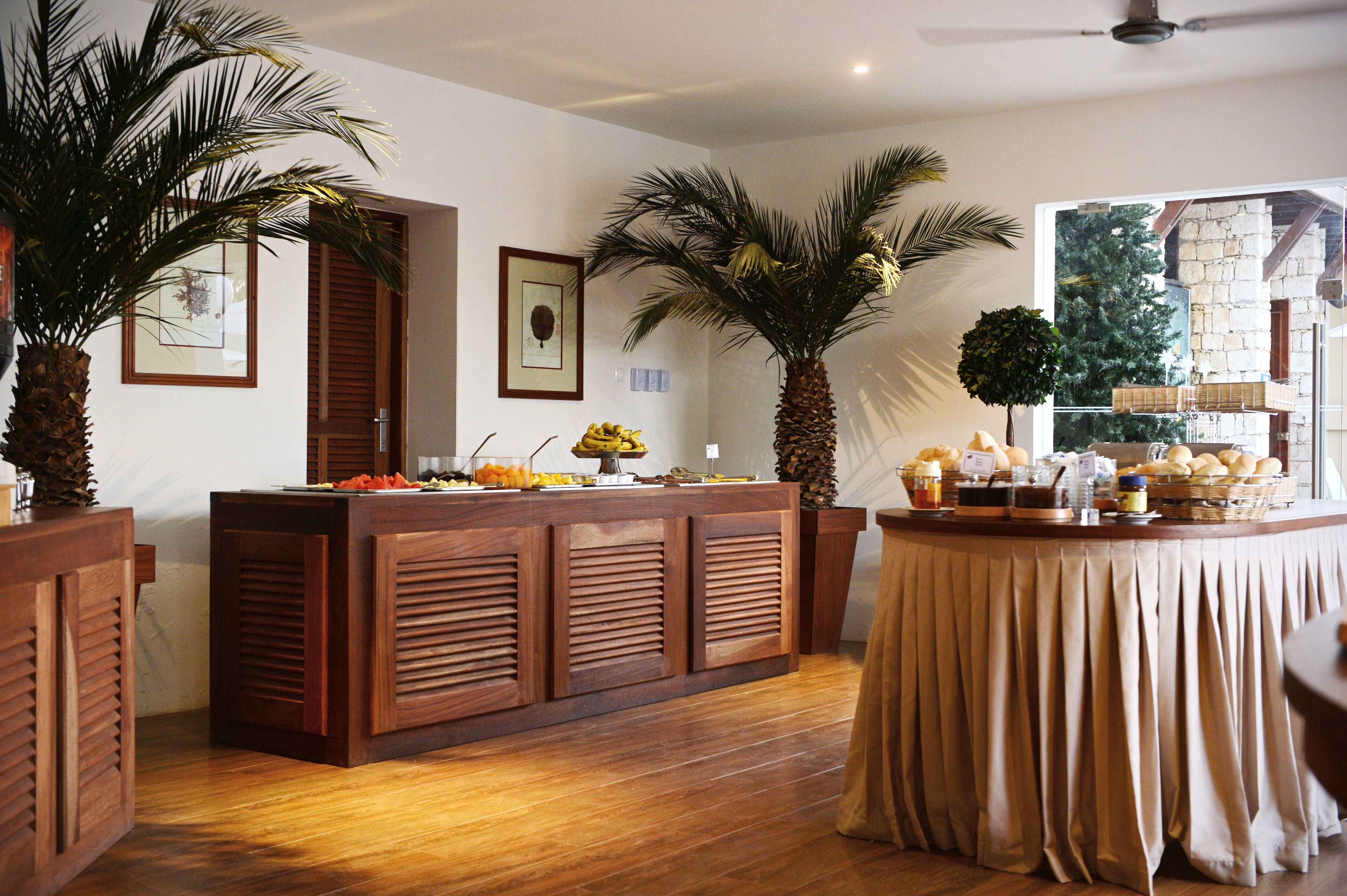 A reception area with a wooden counter, palm trees, and a view of a stone building through a window.