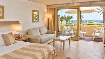 Una habitación de hotel con cama, sofá, mesa y balcón con sillas y una sombrilla.