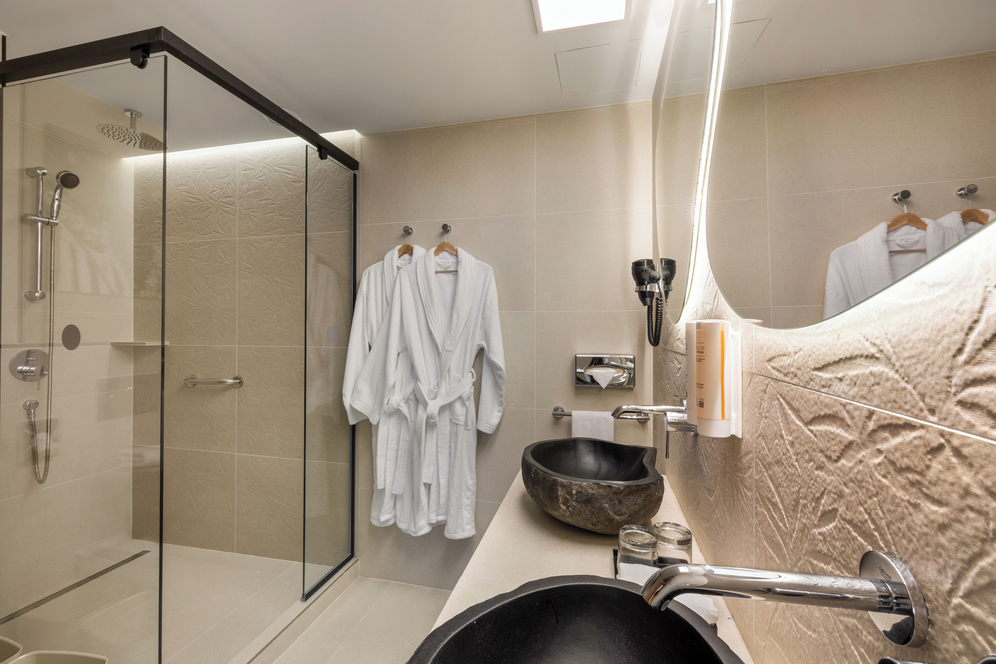 A modern bathroom with a glass-enclosed shower, a large basin sink, and a towel rack with white robes.
