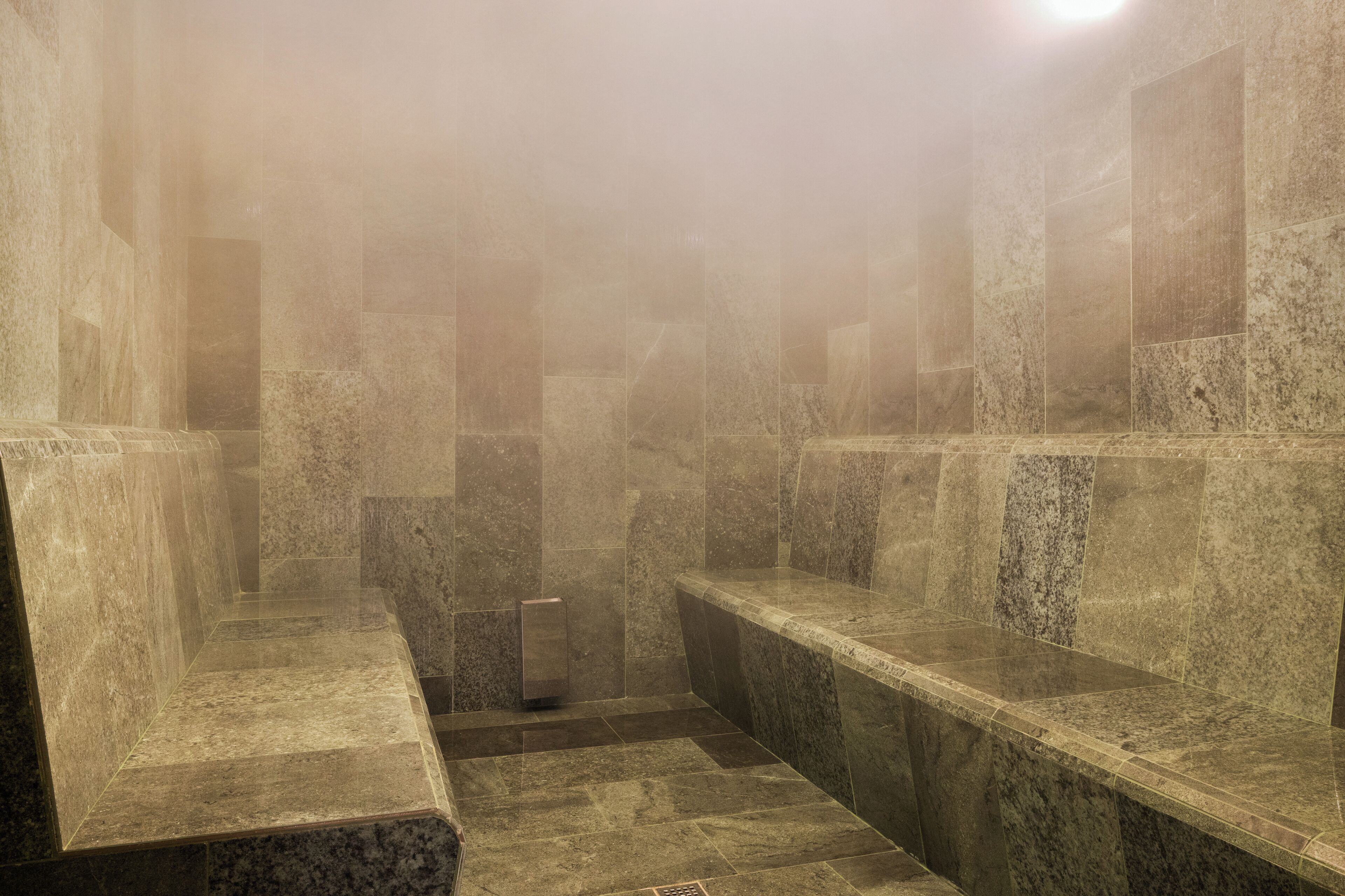 Une salle de bain aux murs en pierre, carrelée, avec des bancs et une colonne centrale.