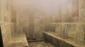 Un baño con paredes de piedra, suelo de baldosas, bancos y una columna central.