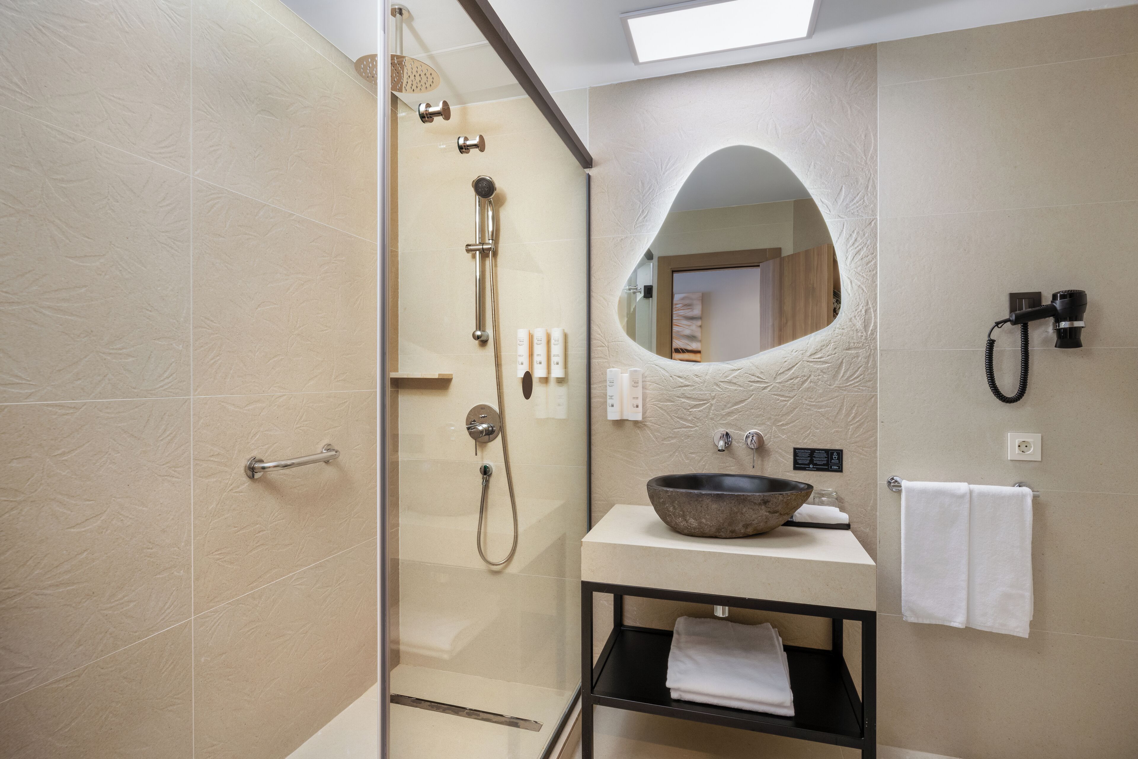 A modern bathroom with a glass-enclosed shower, a sink with a bowl basin, a mirror, and a towel rack.