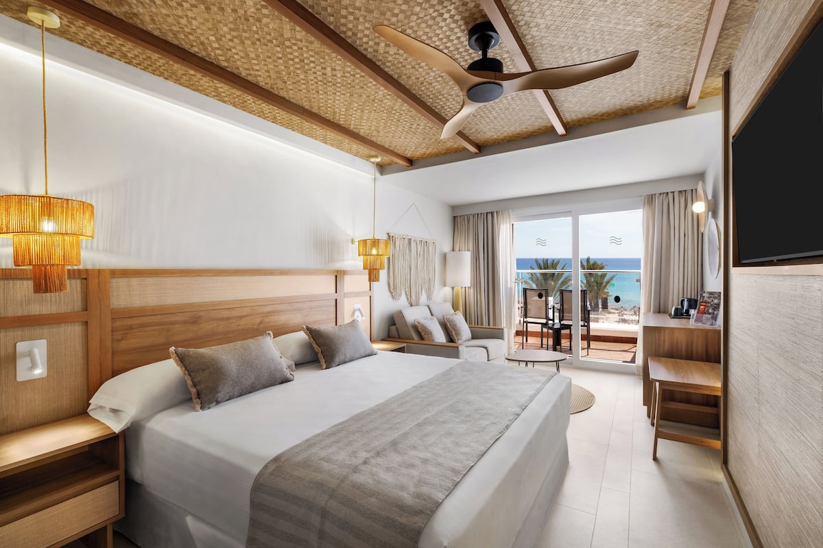 A modern hotel room with a large bed, a ceiling fan, a balcony with a view, and a TV.