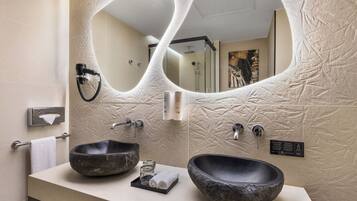 A bathroom with two large stone sinks, a towel rack, a mirror, and a shower area.