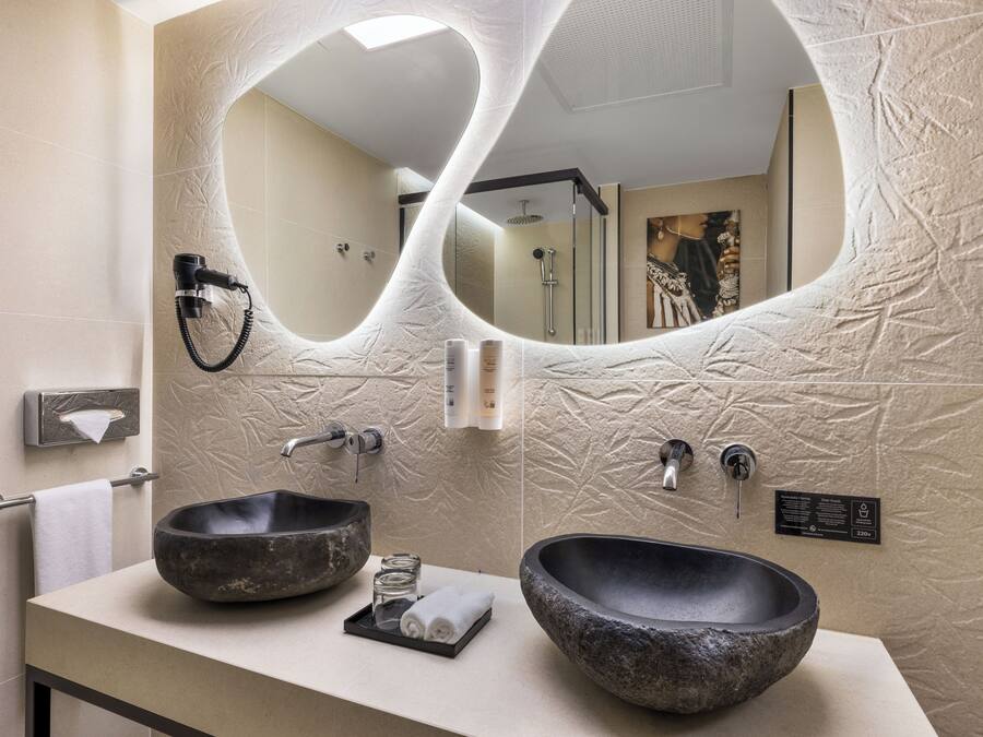 A bathroom with two large stone sinks, a towel rack, a mirror, and a shower area.
