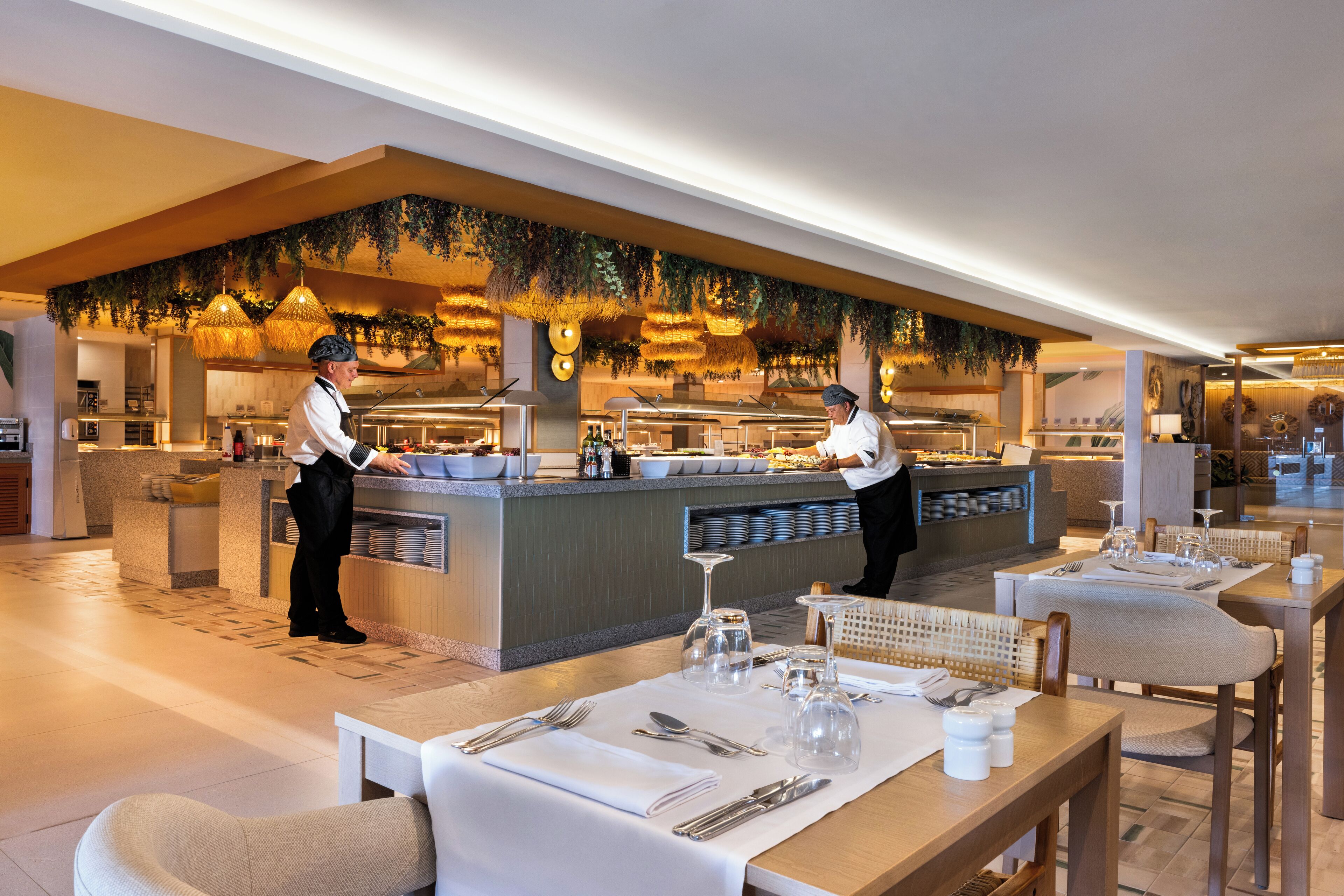 Un restaurante moderno con una zona de bufé, mesas ordenadas con cubiertos y un ambiente cálido y acogedor.