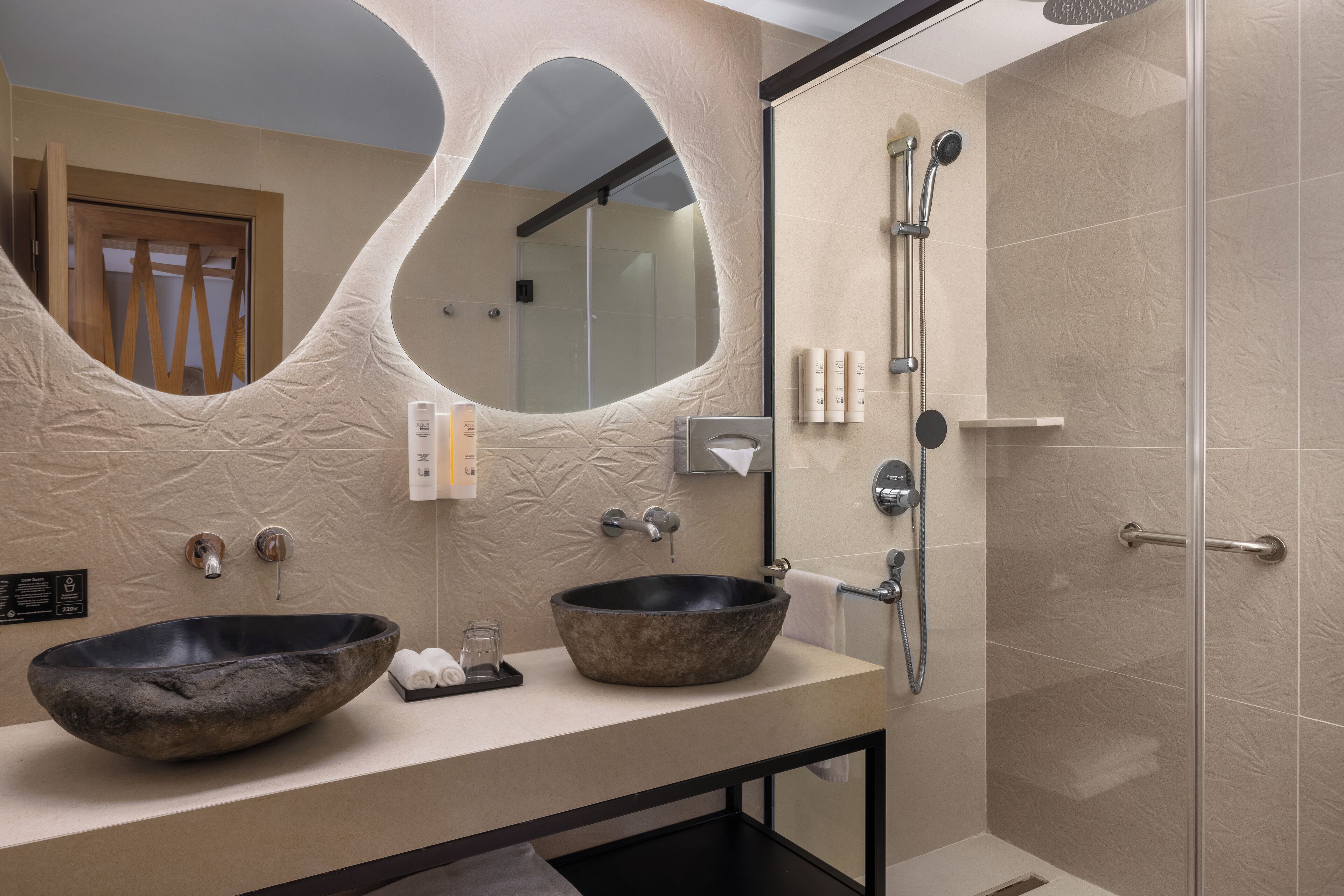 A modern bathroom with two stone sinks, a large mirror, and a glass-enclosed shower.