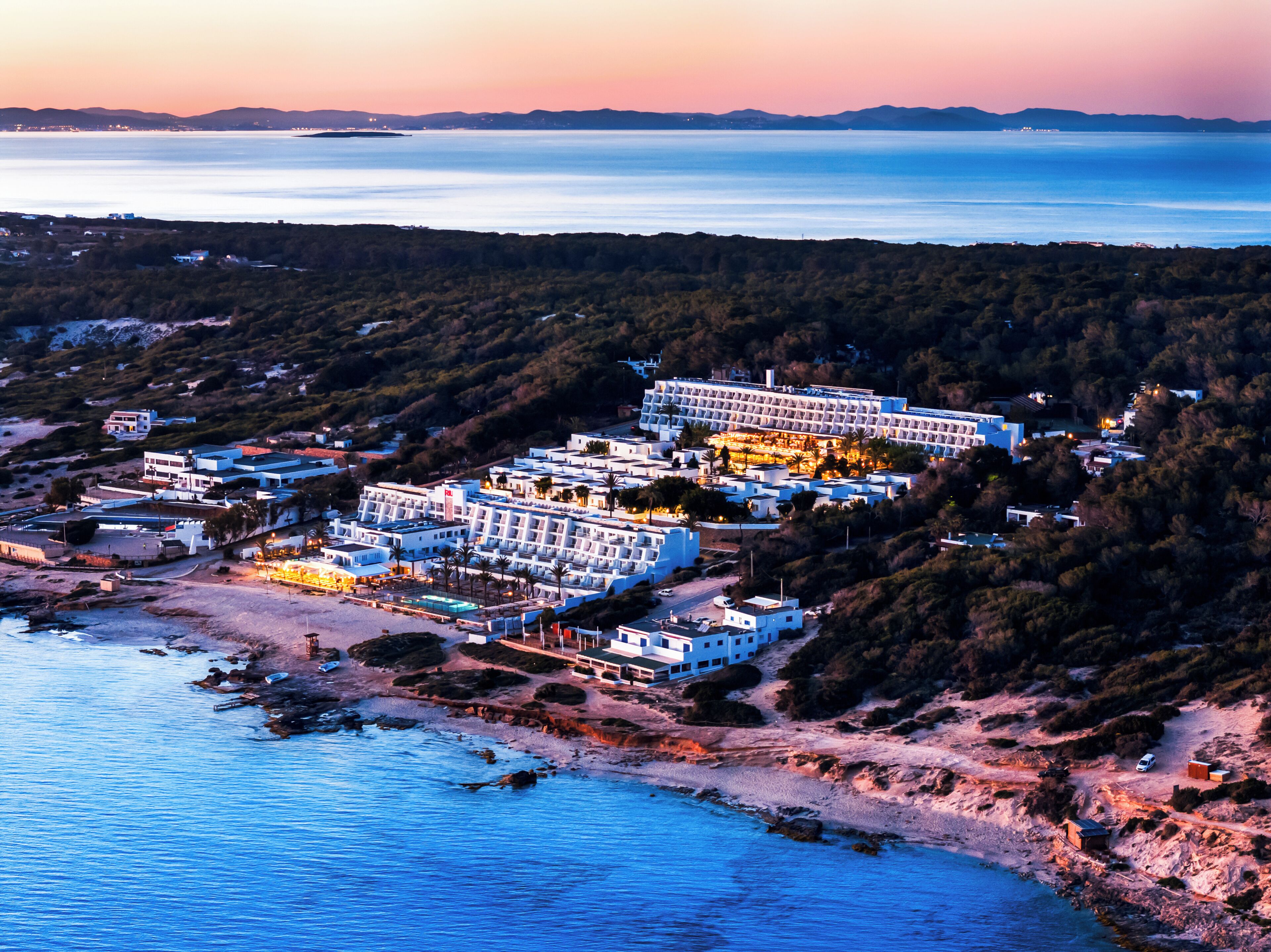 A coastal hotel with multiple buildings, a beach, and a view of the sea.