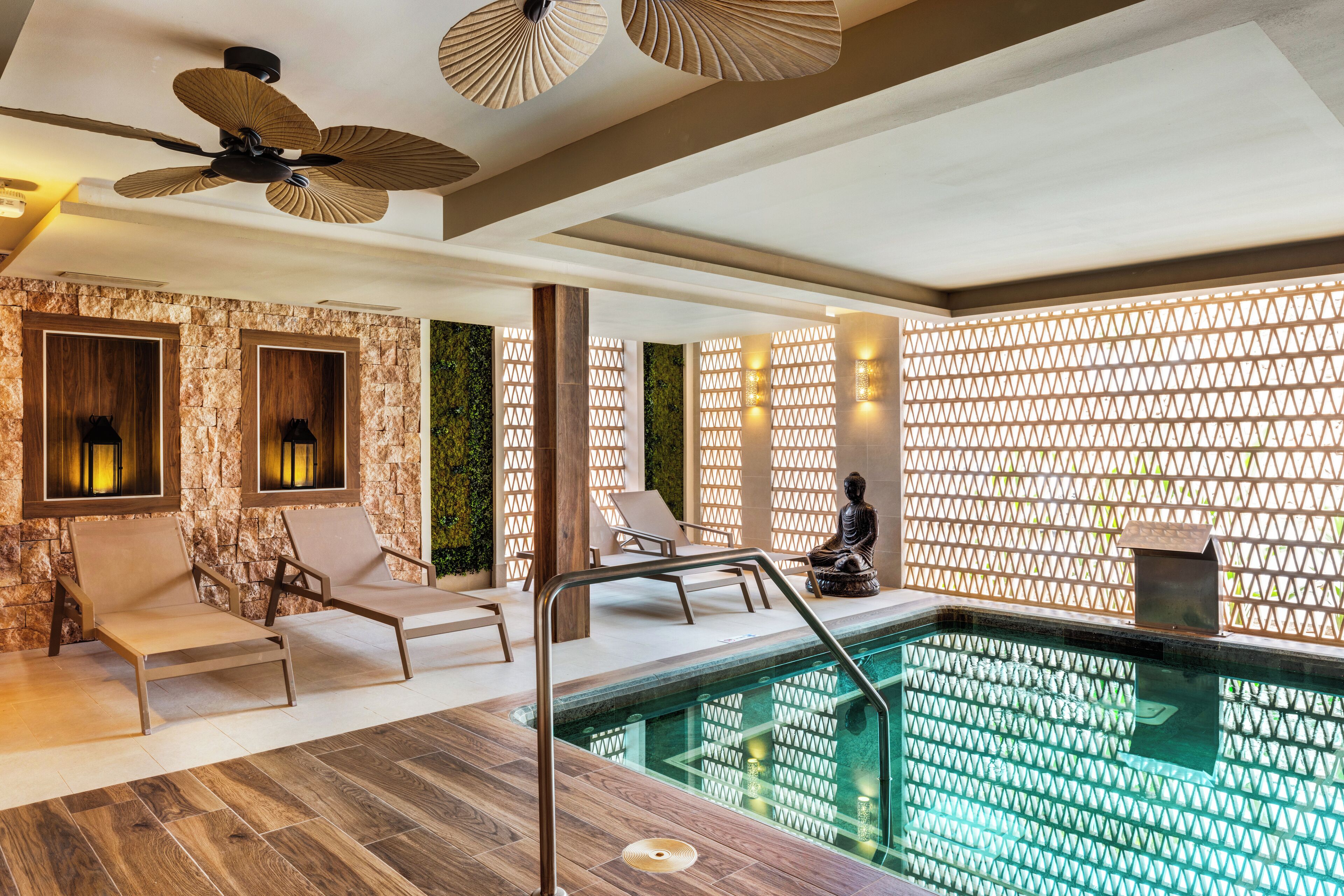 A modern indoor pool area with lounge chairs, a ceiling fan, and decorative lighting.