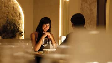 Una mujer sentada a una mesa en una habitación con poca luz, una pared de piedra y un espejo grande.