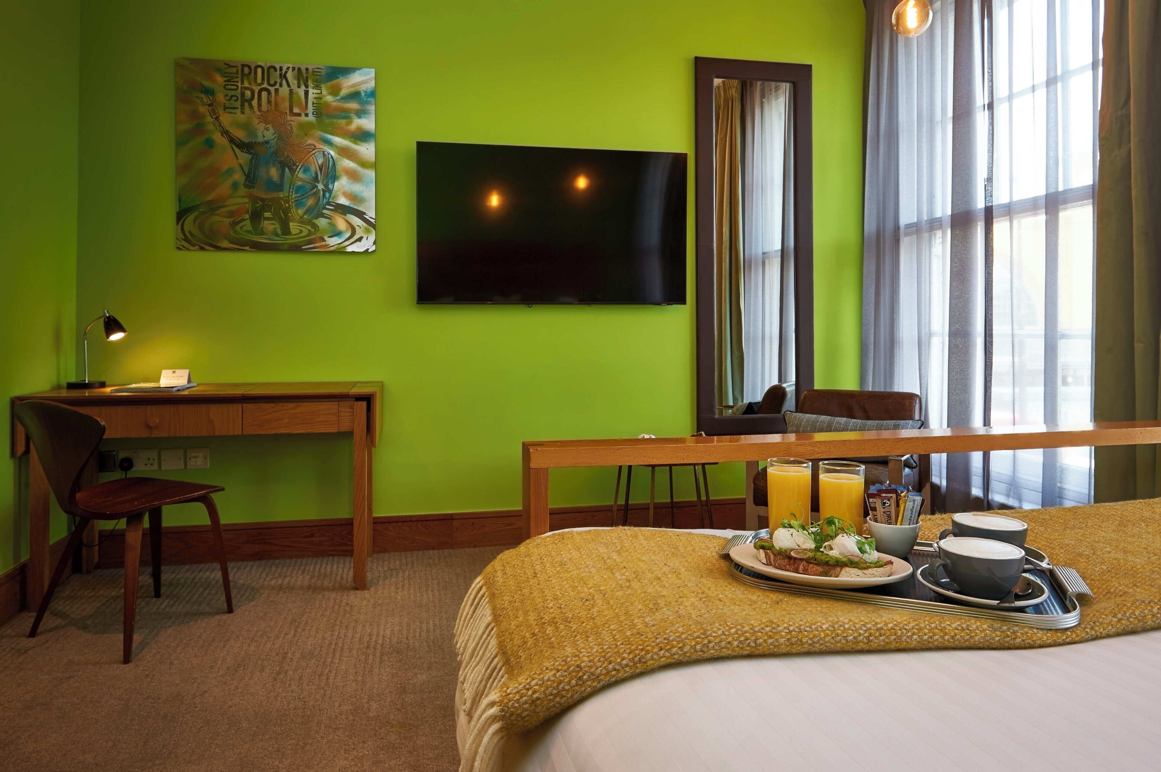 A hotel room with a bed, a desk, a chair, a TV, and a breakfast tray.