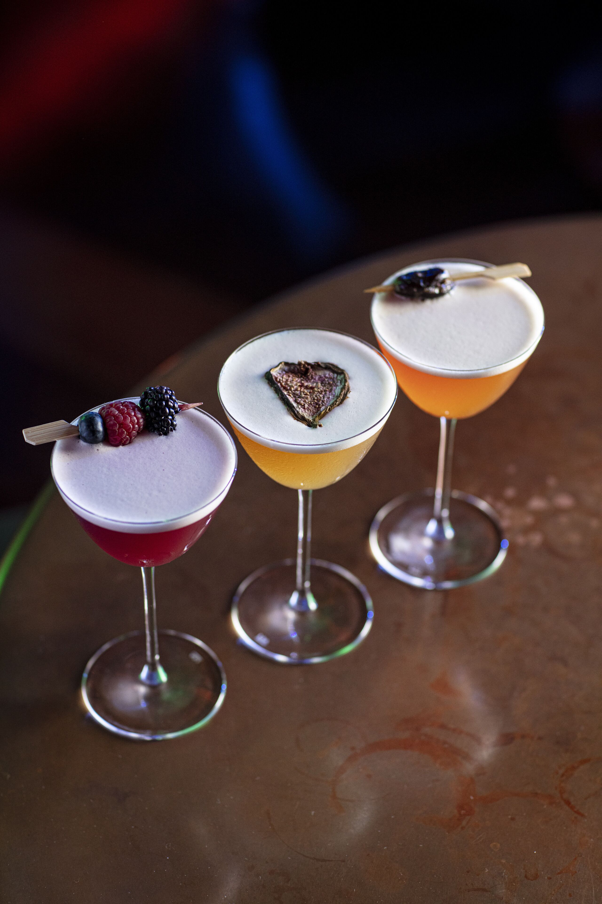 Three cocktails with fruit garnishes on a reflective surface.