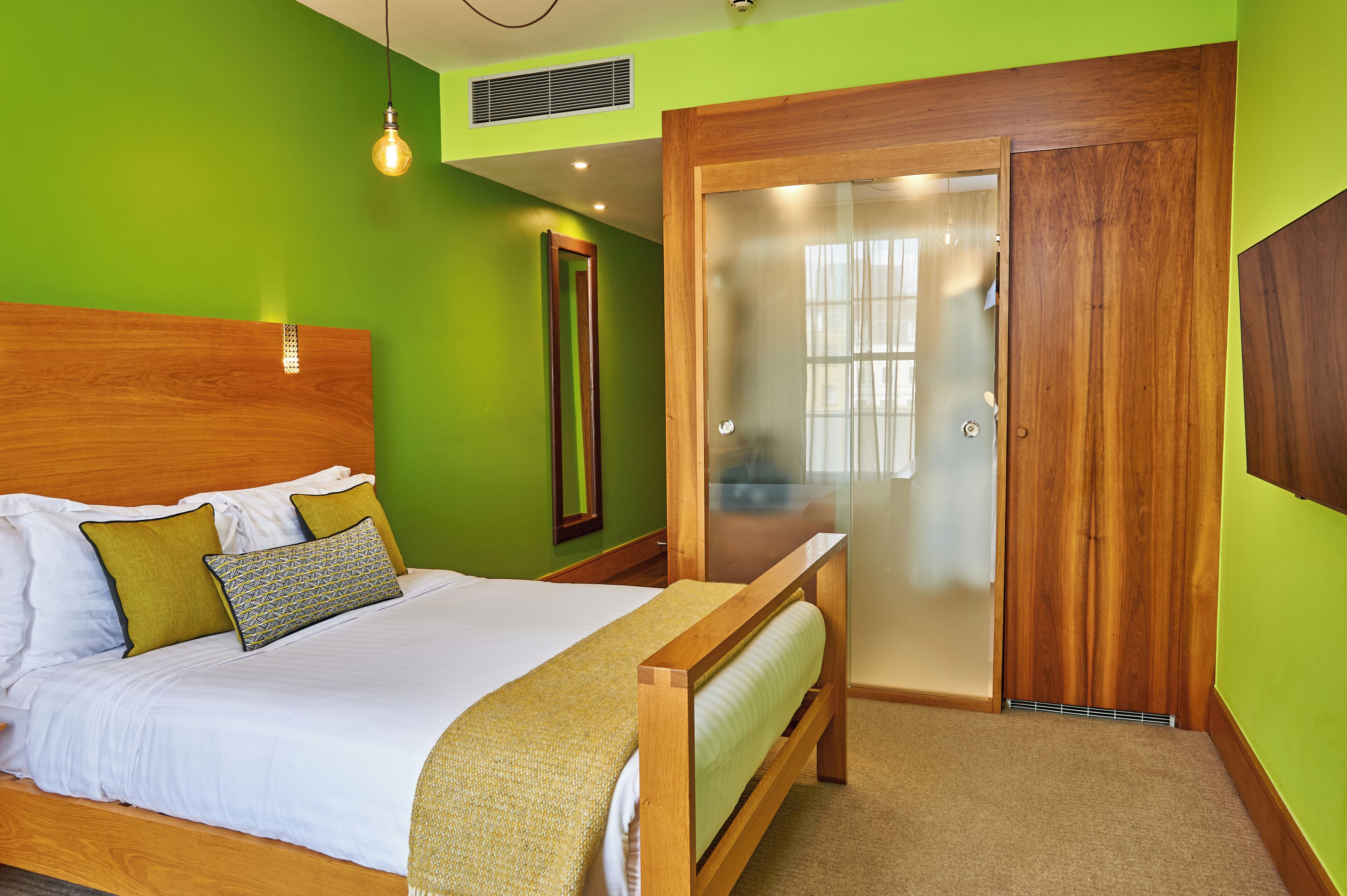 Une chambre à coucher comprenant un lit, une tête de lit en bois, un banc, un miroir et une porte en verre dépoli.