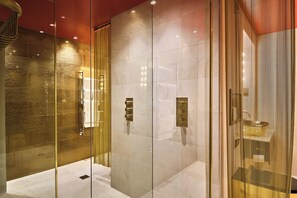 A modern bathroom with glass partitions, a marble floor, and a gold accent wall.