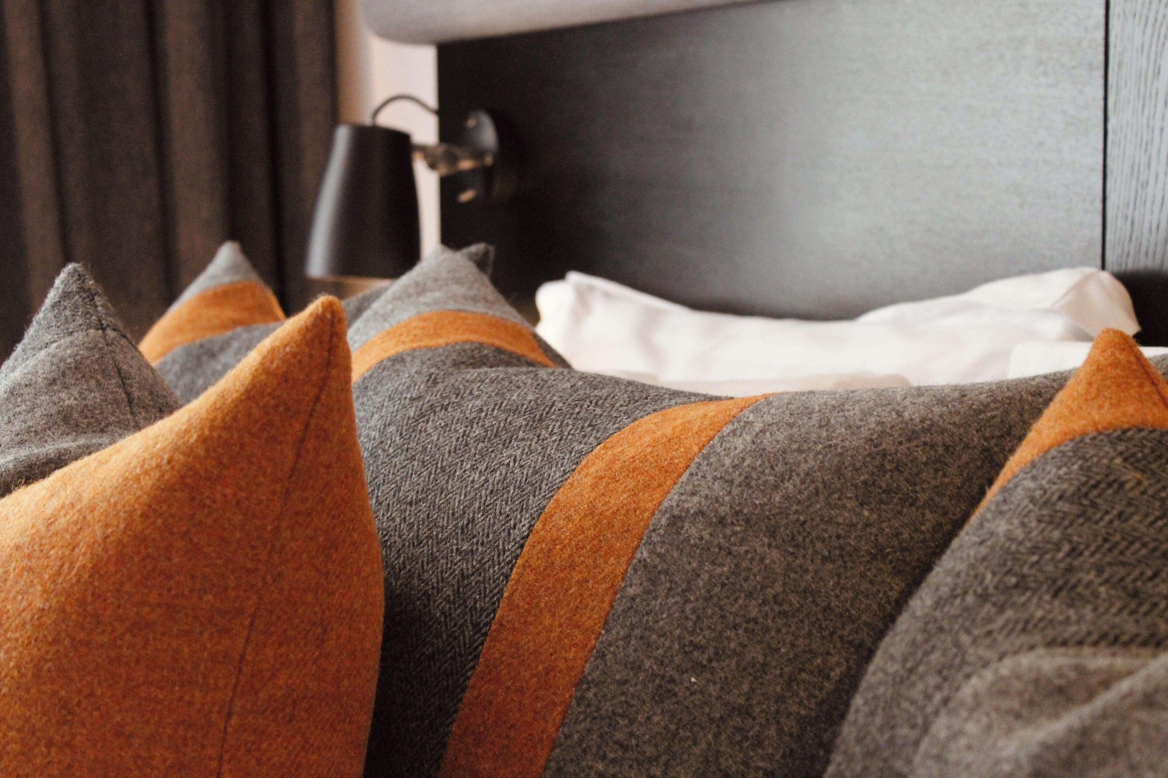 A bed with grey and orange pillows, a white sheet, and a black lamp on a bedside table.