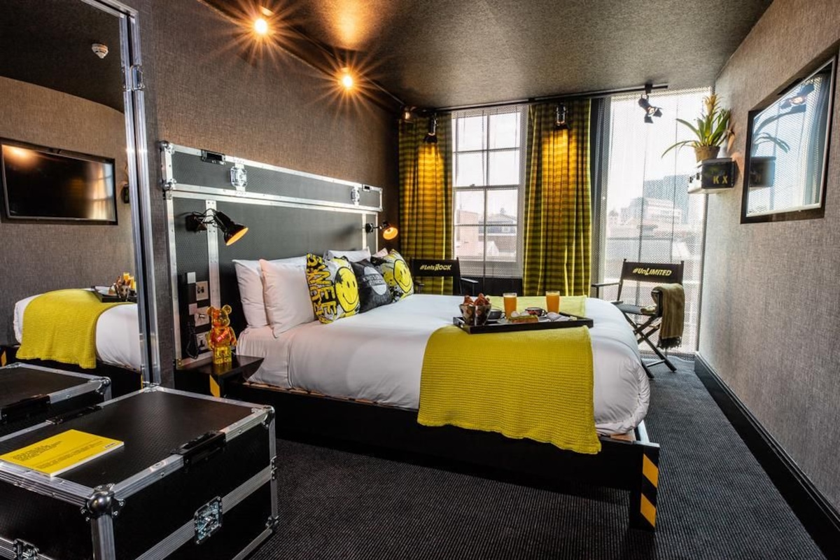 Una habitación de hotel con una cama grande, un escritorio, una maleta y una ventana con cortinas.