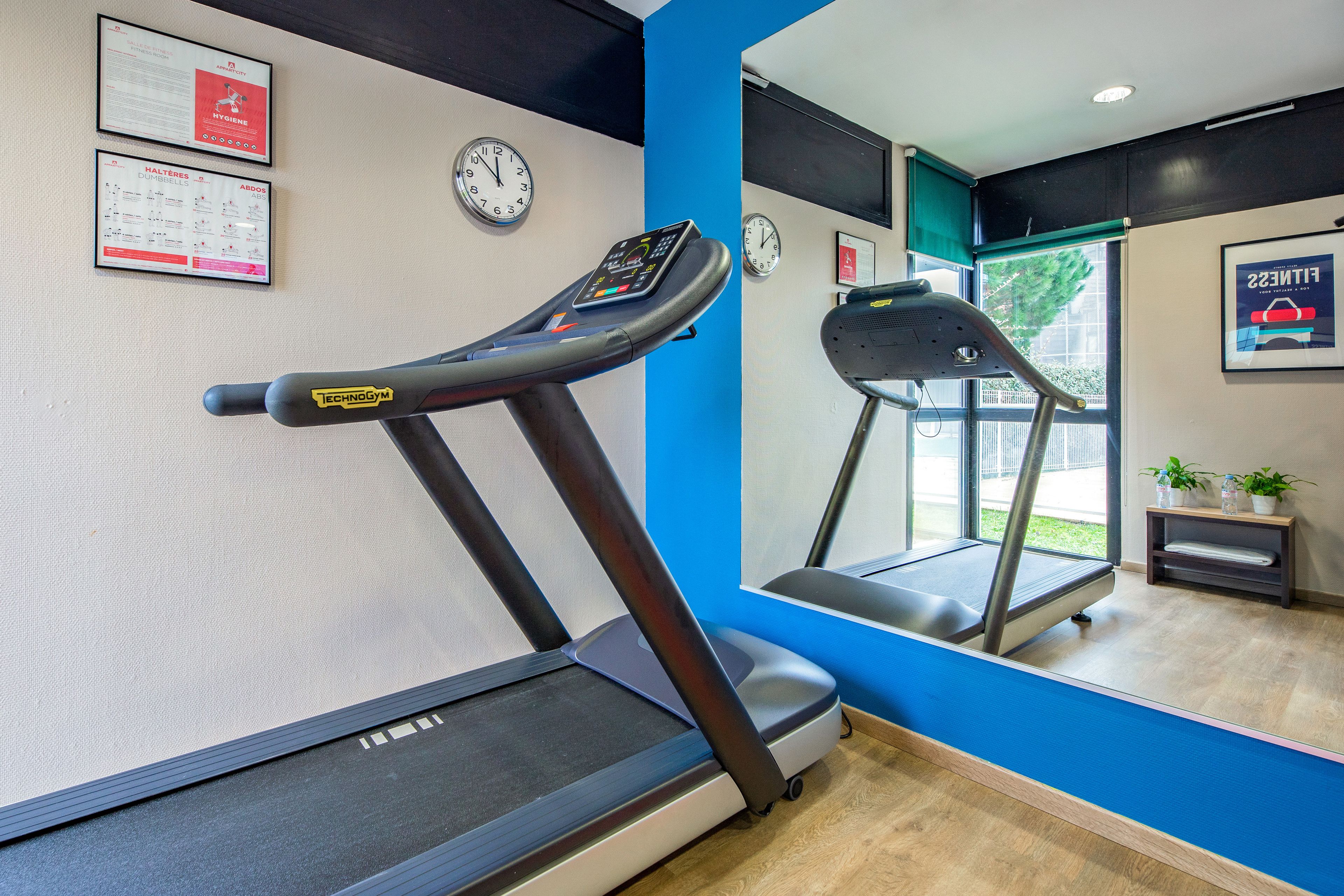 A gym with treadmills, a wall clock, and a framed poster.