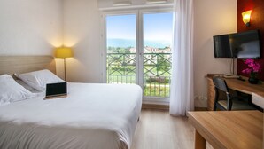 Habitación de hotel con cama, escritorio con silla, televisor y balcón con vistas a edificios.