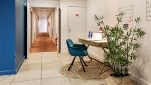 Un pasillo con una pared azul, una puerta de madera, un escritorio con una silla y una planta grande en maceta.