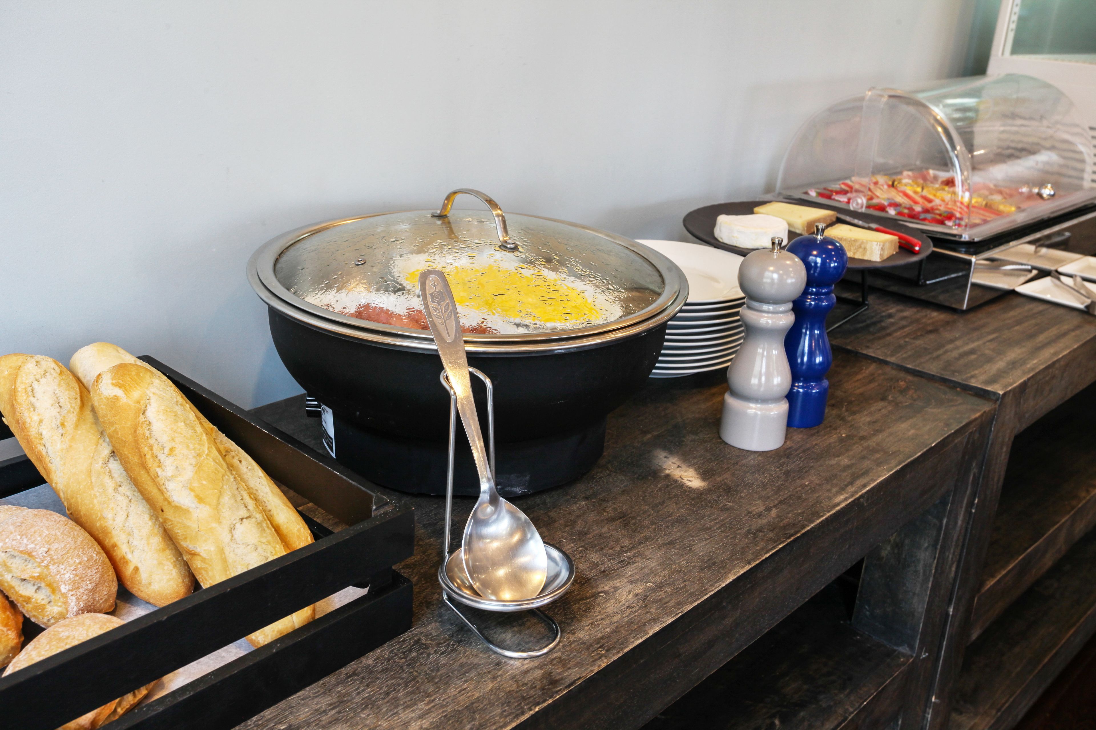 A buffet setup with a large pot of soup, bread, and condiments.