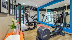 Un gimnasio con máquinas de cardio, un espejo y una botella de agua sobre un banco.