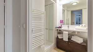 Un baño moderno con cabina de ducha de vidrio, un lavabo blanco con espejo y un mueble de madera debajo.