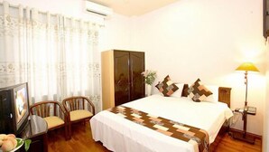 Quarto de hotel com uma cama grande, um guarda-roupa, uma escrivaninha com cadeira e uma televisão.