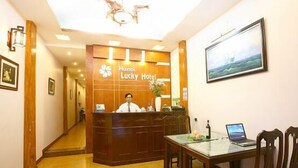 Balcão de recepção no Hanoi Lucky Hotel, com um recepcionista, um laptop e uma área de refeições com cadeiras e mesa.
