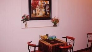 Uma sala de jantar com uma mesa e quatro cadeiras, um quadro emoldurado acima da mesa e dois vasos com flores em cada lado.