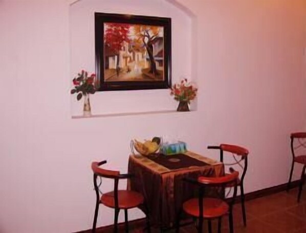 Un comedor con una mesa y cuatro sillas, un cuadro enmarcado sobre la mesa, y dos jarrones con flores a cada lado.