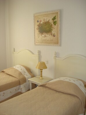 Une chambre avec deux lits simples, une table de chevet avec une lampe et une illustration botanique accrochée au mur.