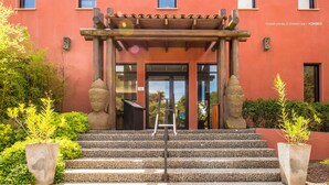A building entrance with a wooden pergola, stone statues, and a staircase leading to the door. - Hôtel restaurant spa Disini Montpellier Est, The Originals Relais (Castries)