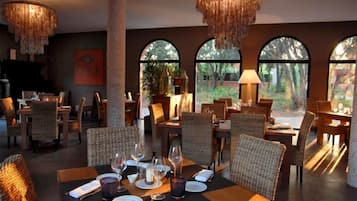 A restaurant with wicker furniture, round tables, and a chandelier.