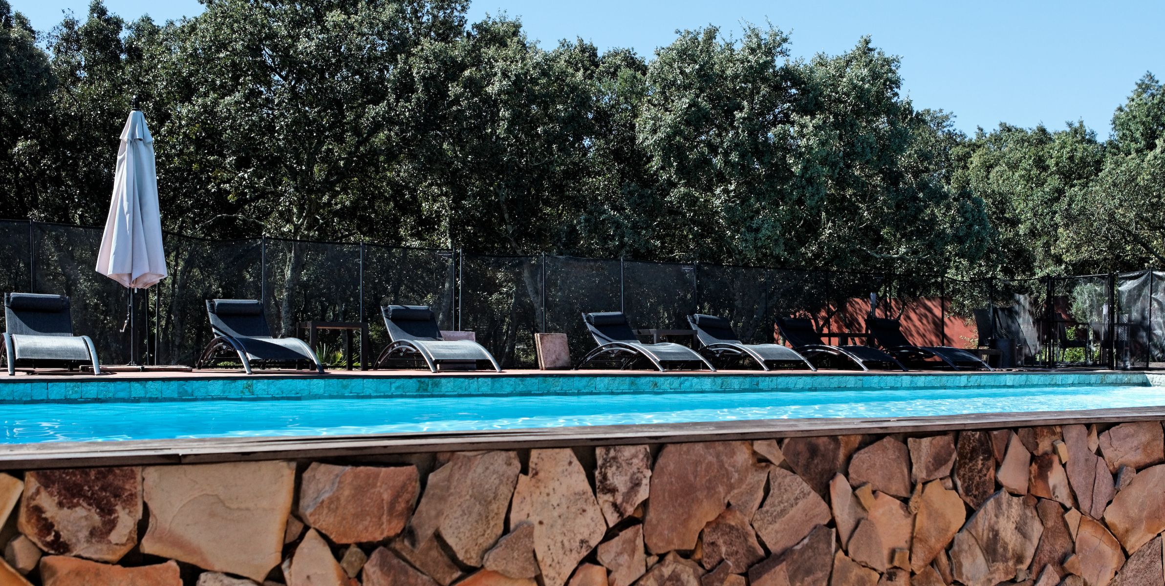 Una piscina con sillones de descanso y un muro de piedra.