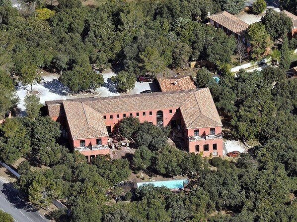A large, multi-story building with a tiled roof, surrounded by dense trees.