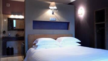 Habitación de hotel con cama, mesita de noche, espejo y lámpara de pared.