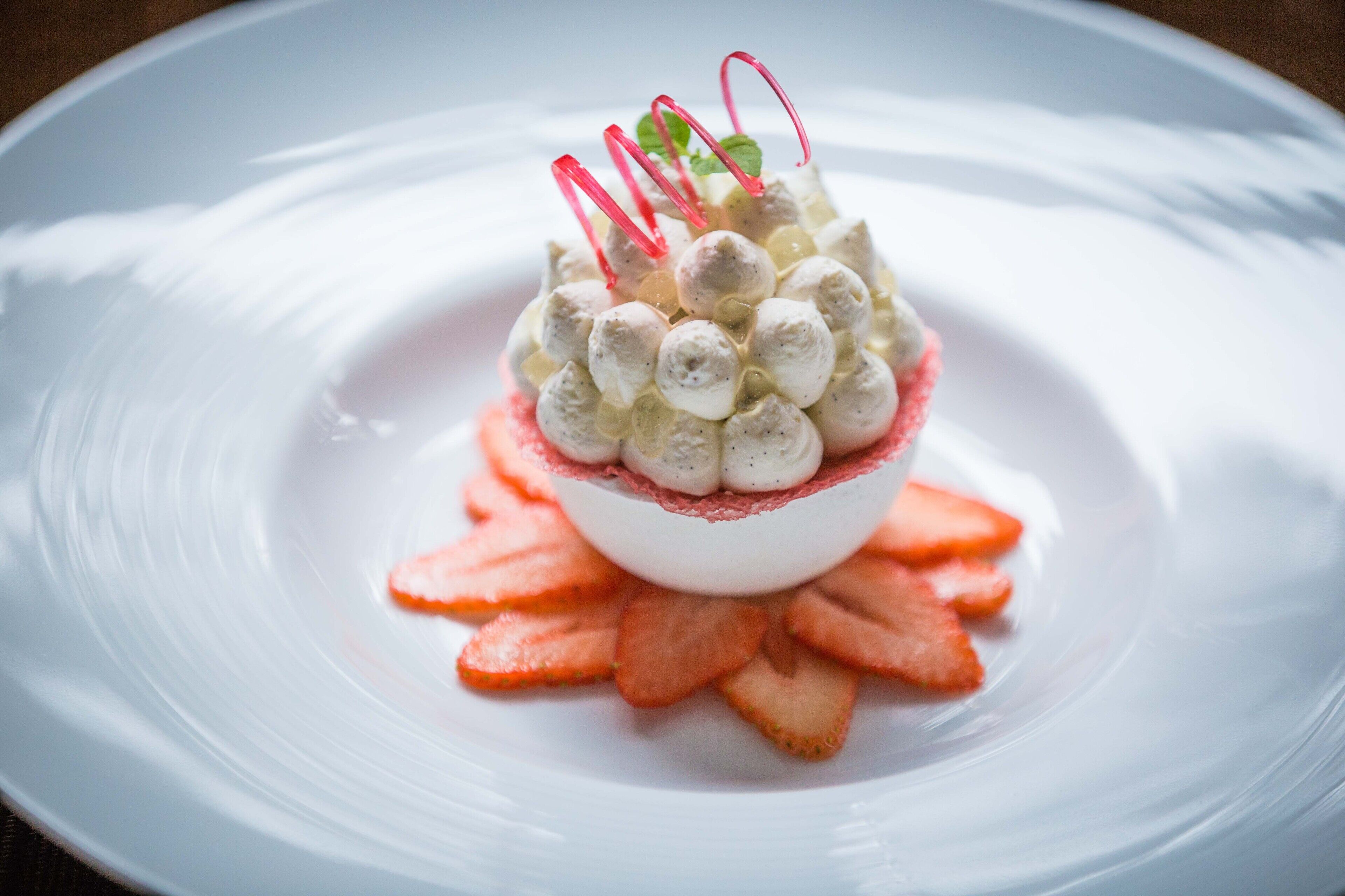A dessert on a white plate with strawberries and a decorative element.
