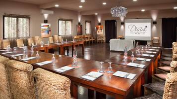 A conference room with long tables, wicker chairs, and a projector screen displaying 'Disini Hotel Restaurant Spa'.