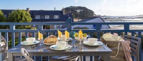 Ein Tisch ist für das Frühstück gedeckt, mit Blick auf das Meer und Gebäude im Hintergrund.
