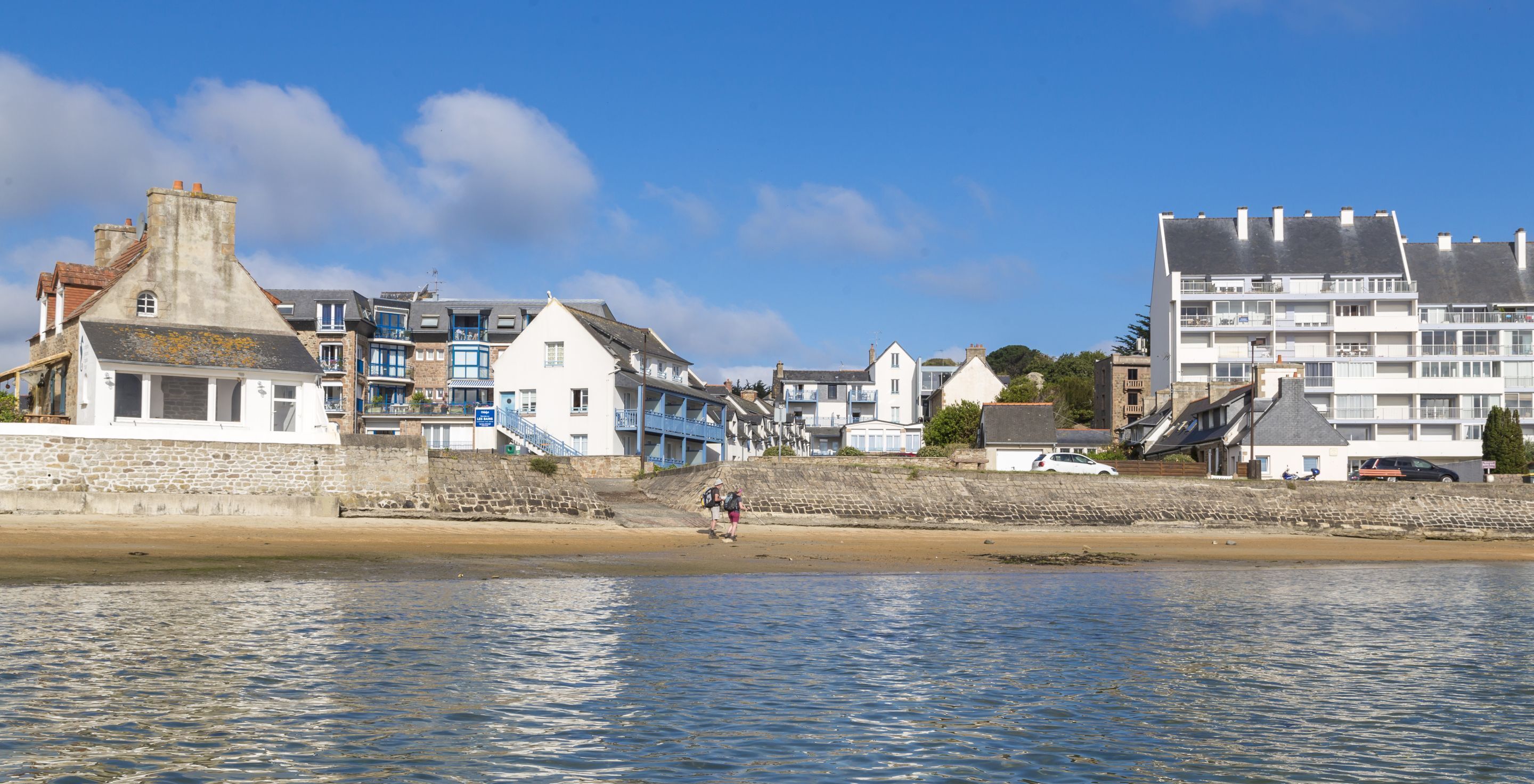 A coastal town with buildings along the waterfront, including a stone wall and a beach.