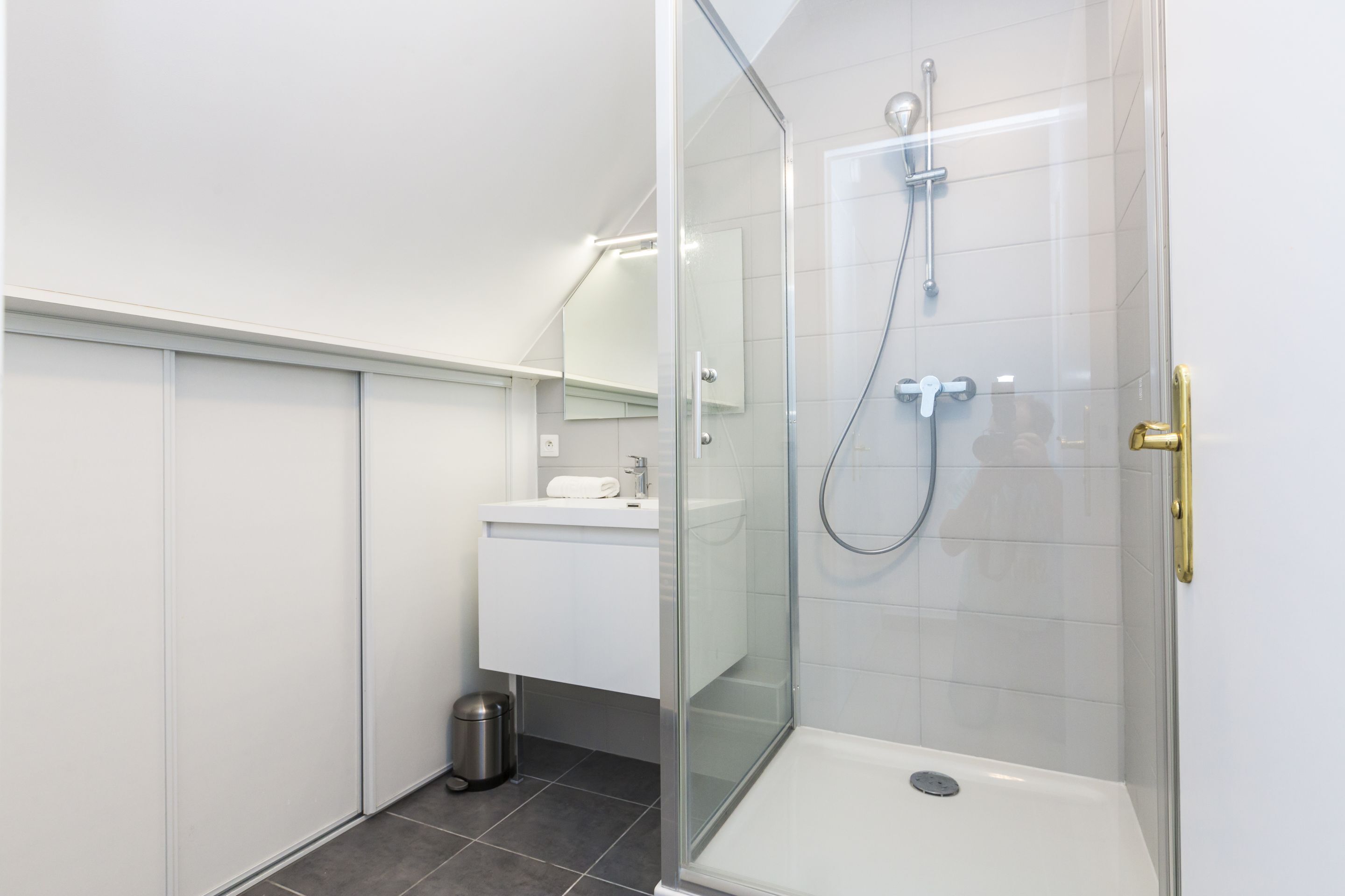 Een moderne badkamer met een douchecabine van glas, een witte wastafel en een spiegel.