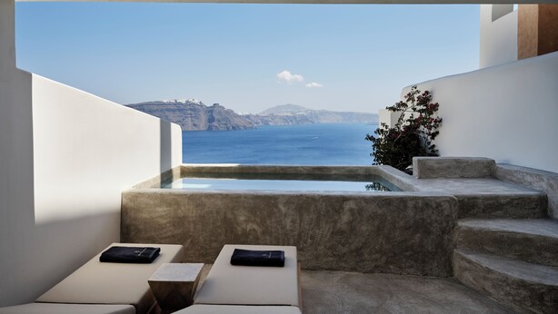 Una terraza moderna al aire libre con piscina, dos sillones de descanso y vistas al mar y acantilados lejanos.