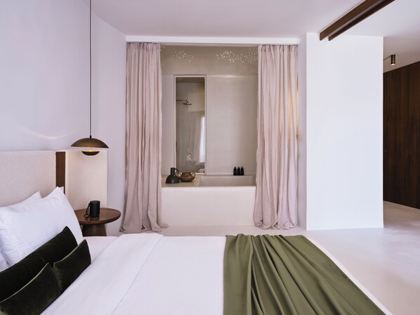 Un dormitorio moderno con una cama grande, una mesita de noche y vistas a un baño con bañera y ducha.