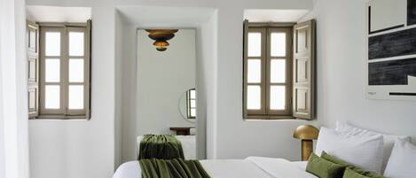 Un dormitorio con una cama grande, dos ventanas con contraventanas abiertas, un espejo y un cuadro en la pared.