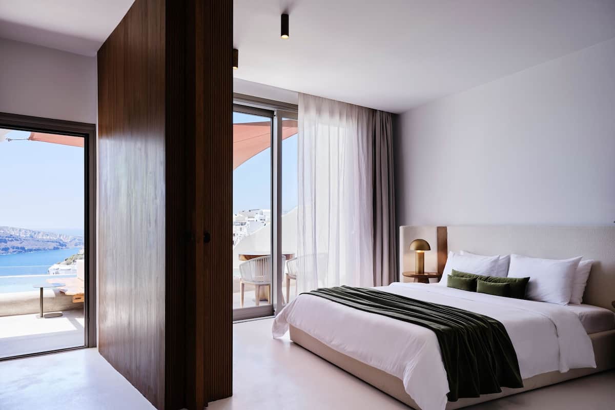 A modern hotel room with a large bed, a nightstand, a lamp, and a view of the sea.