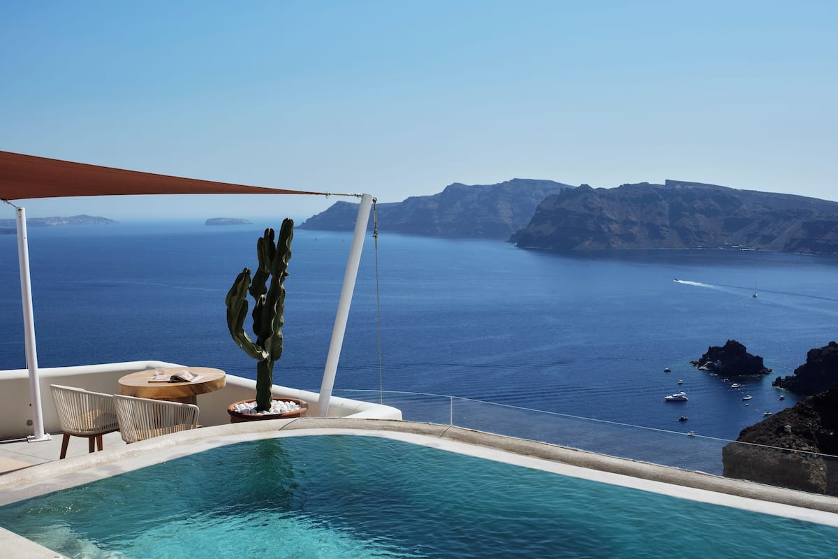 A pool with a cactus, chairs, and a view of the sea and cliffs.
