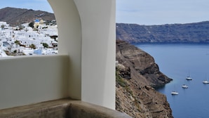 Vista desde un balcón con una bañera de piedra, con vistas a un pueblo costero de edificios blancos y barcos en el agua.
