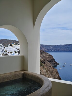 A view from a balcony with a stone bathtub, overlooking a coastal town with white buildings and boats on the water. - Andronis Luxury Suites (Santorini)